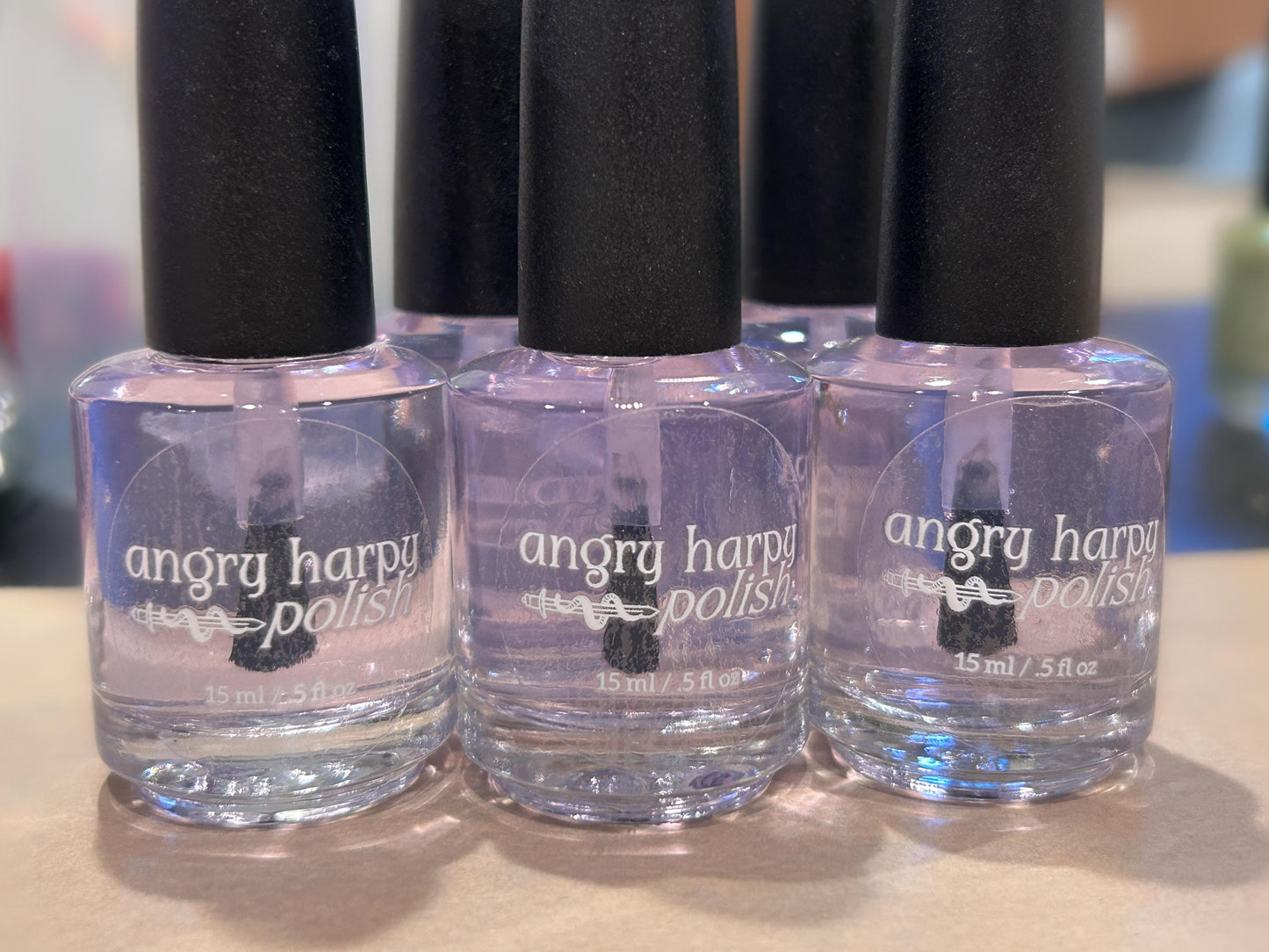 a row of nail polish bottles is lined up filled with clear liquid. the label on each bottle has the Angry Harpy Polish logo.