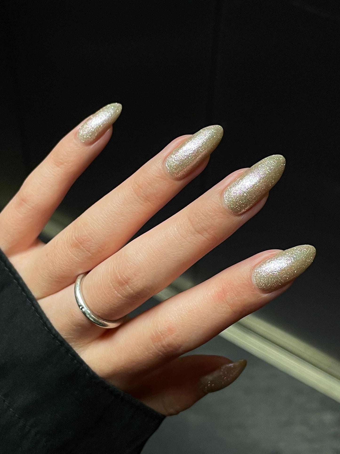 An elegant hand with long nails painted in a sparkly pale khaki color.