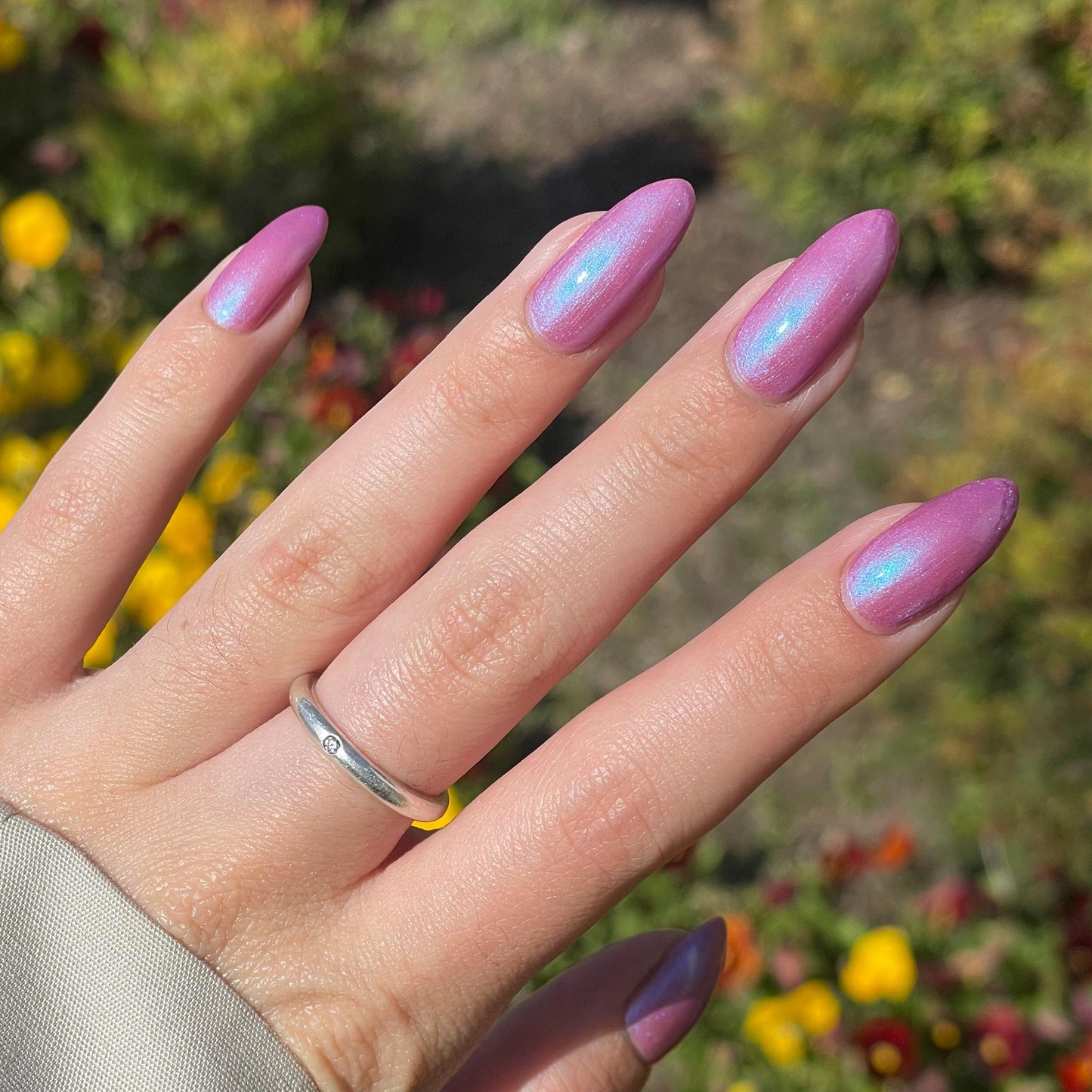 A hand with long nails is painted a purple mauve color with blue shimmer that appears to glow in the sunlight.