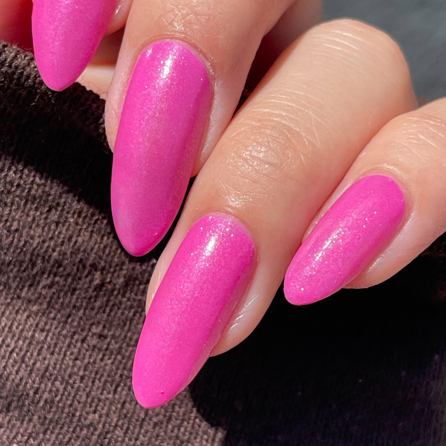 Long nails showcase a bright pink with a slight purple hue glittering in the sun.