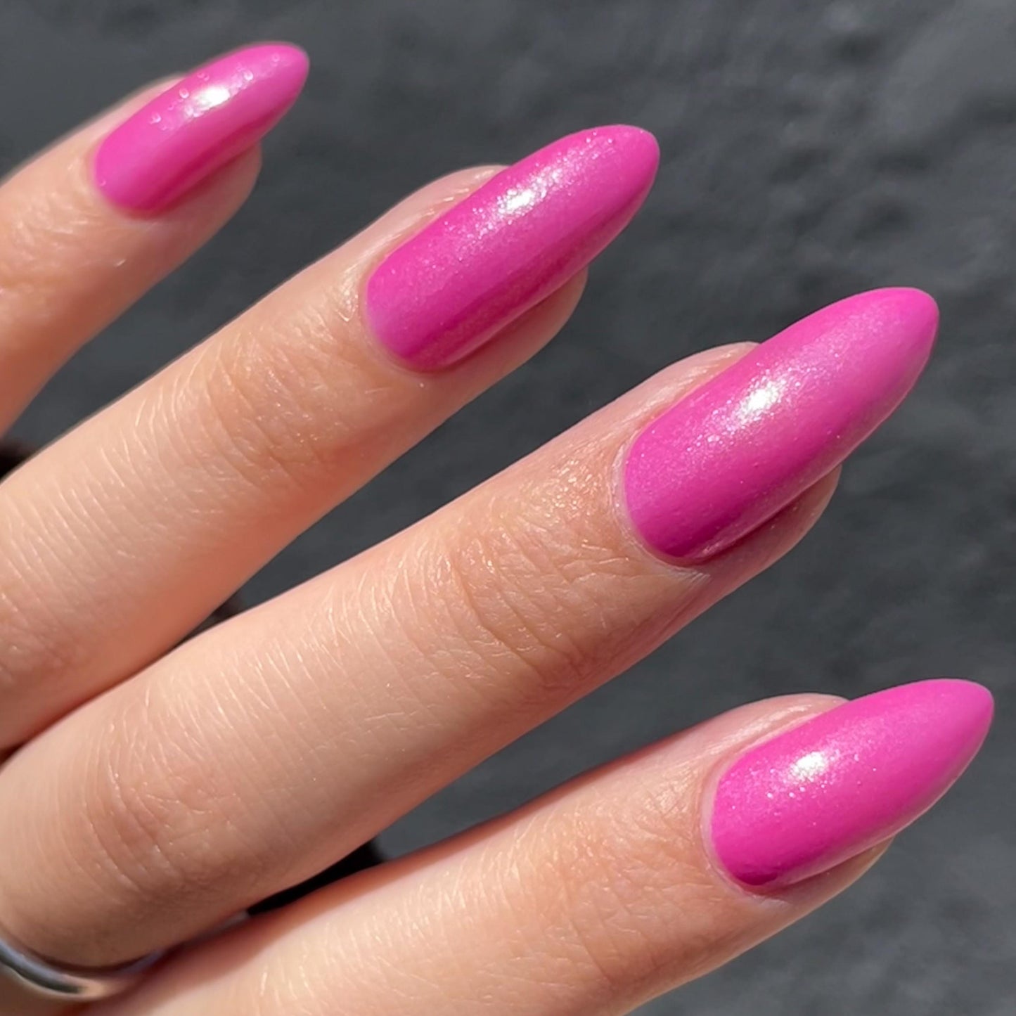 Long nails showcase a bright pink with a slight purple hue glittering in the sun.