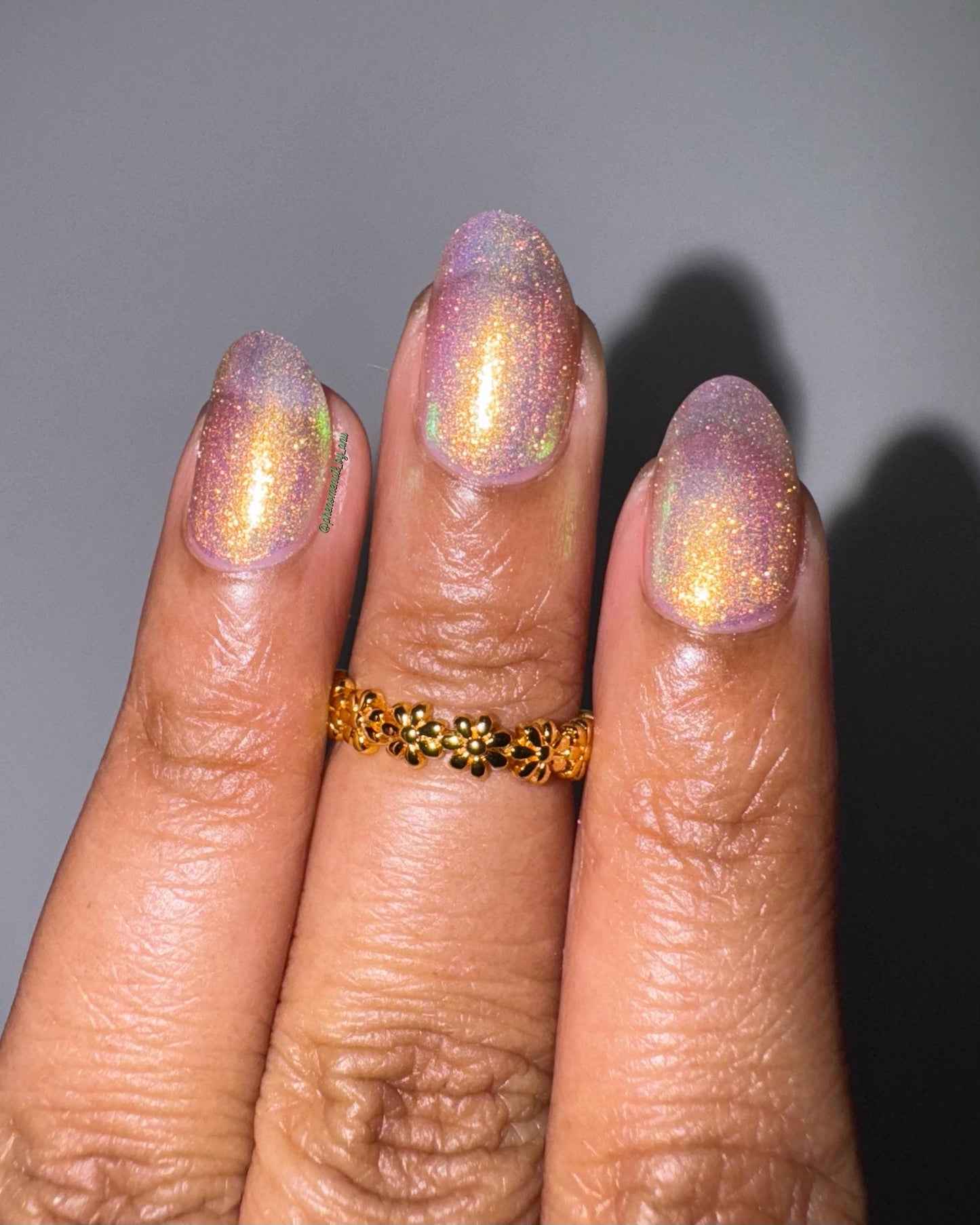 Lit by bright flash, three elegant fingers show off nails painted in a bright shifty polish that seems to glow pink and gold from within.