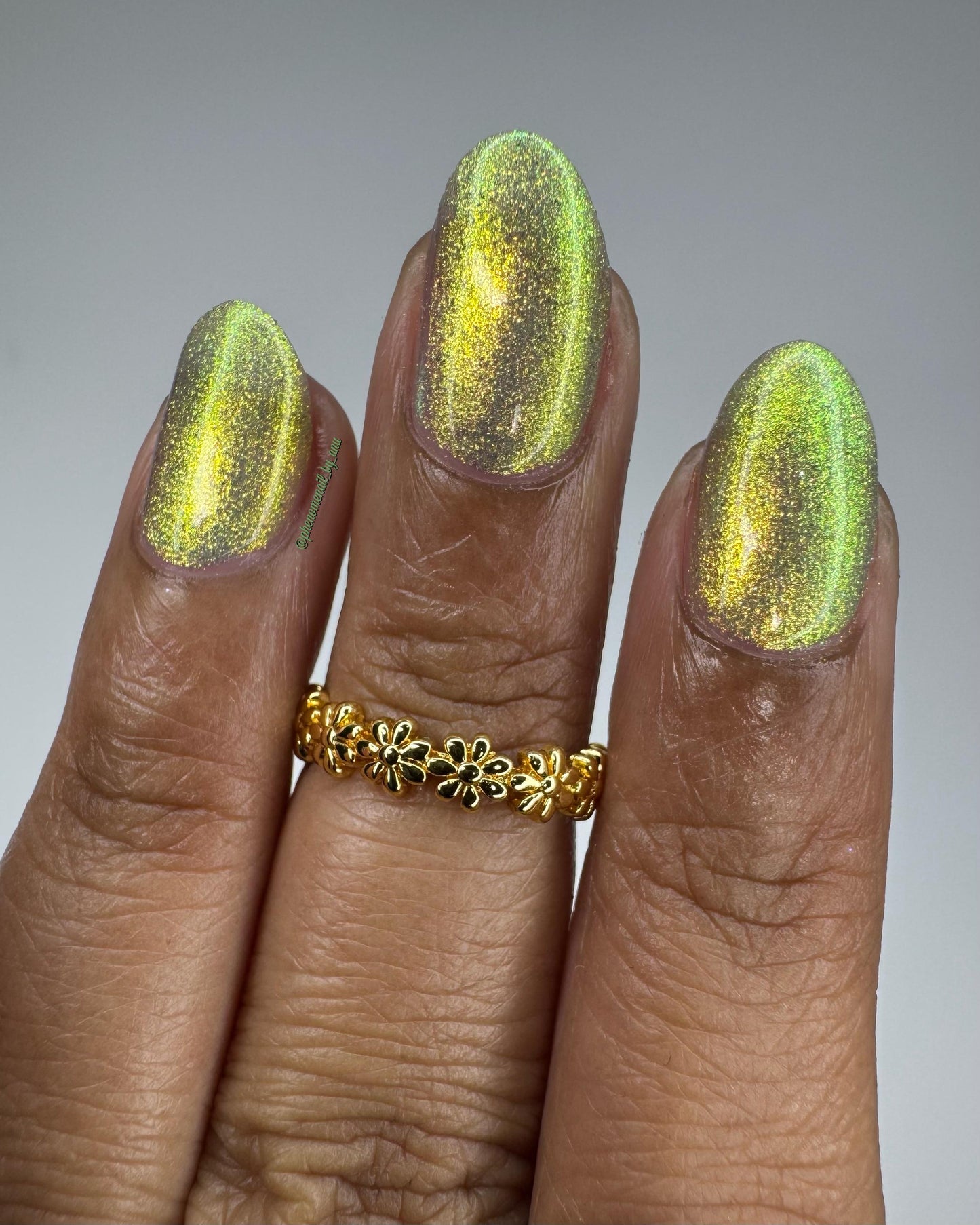 Three elegant fingers show off nails painted in a bright shifty polish that seems to glow yellow-green from within.