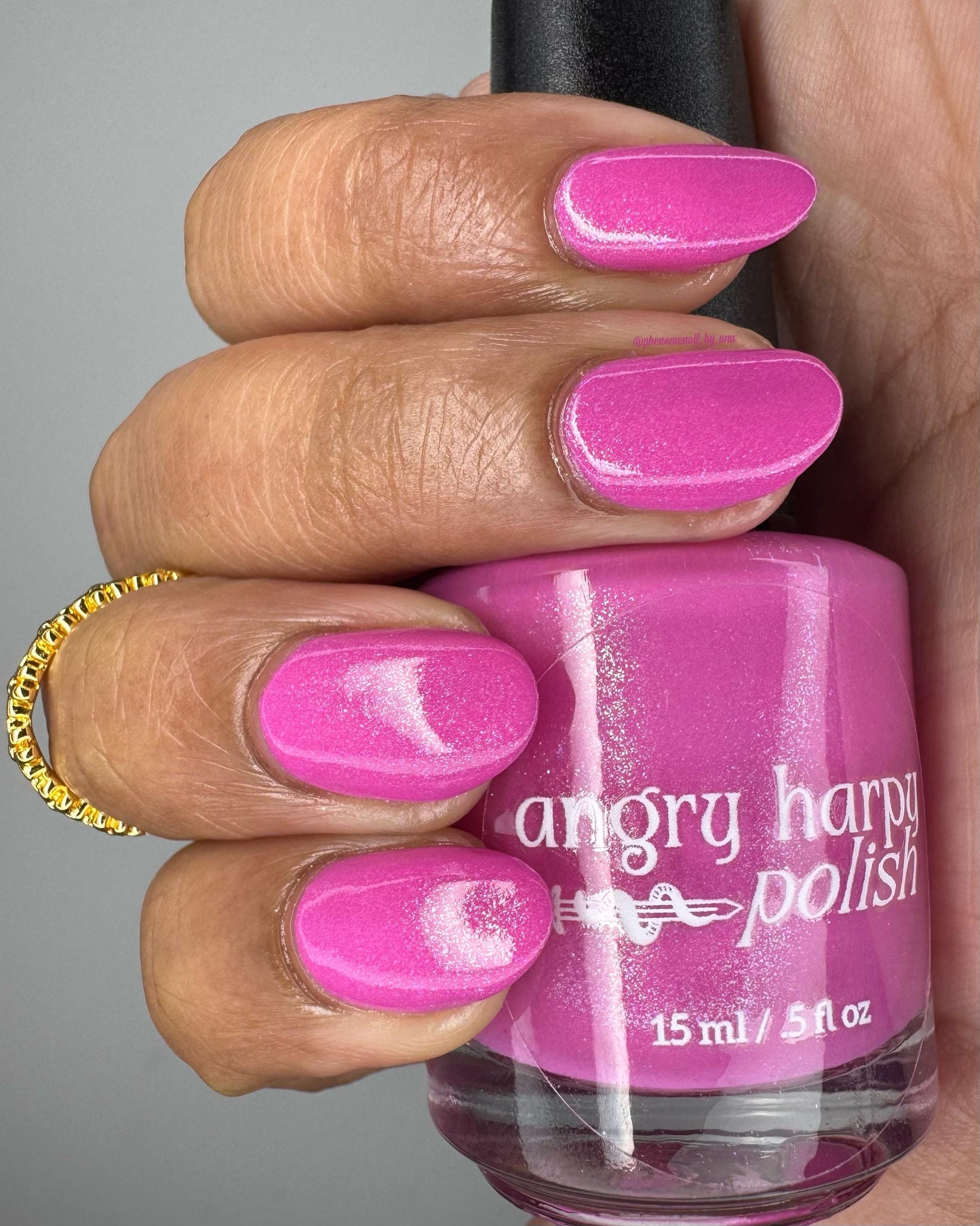 Medium-brown fingers are painted with a blue-leaning pink shimmer polish and hold a bottle of the same polish.