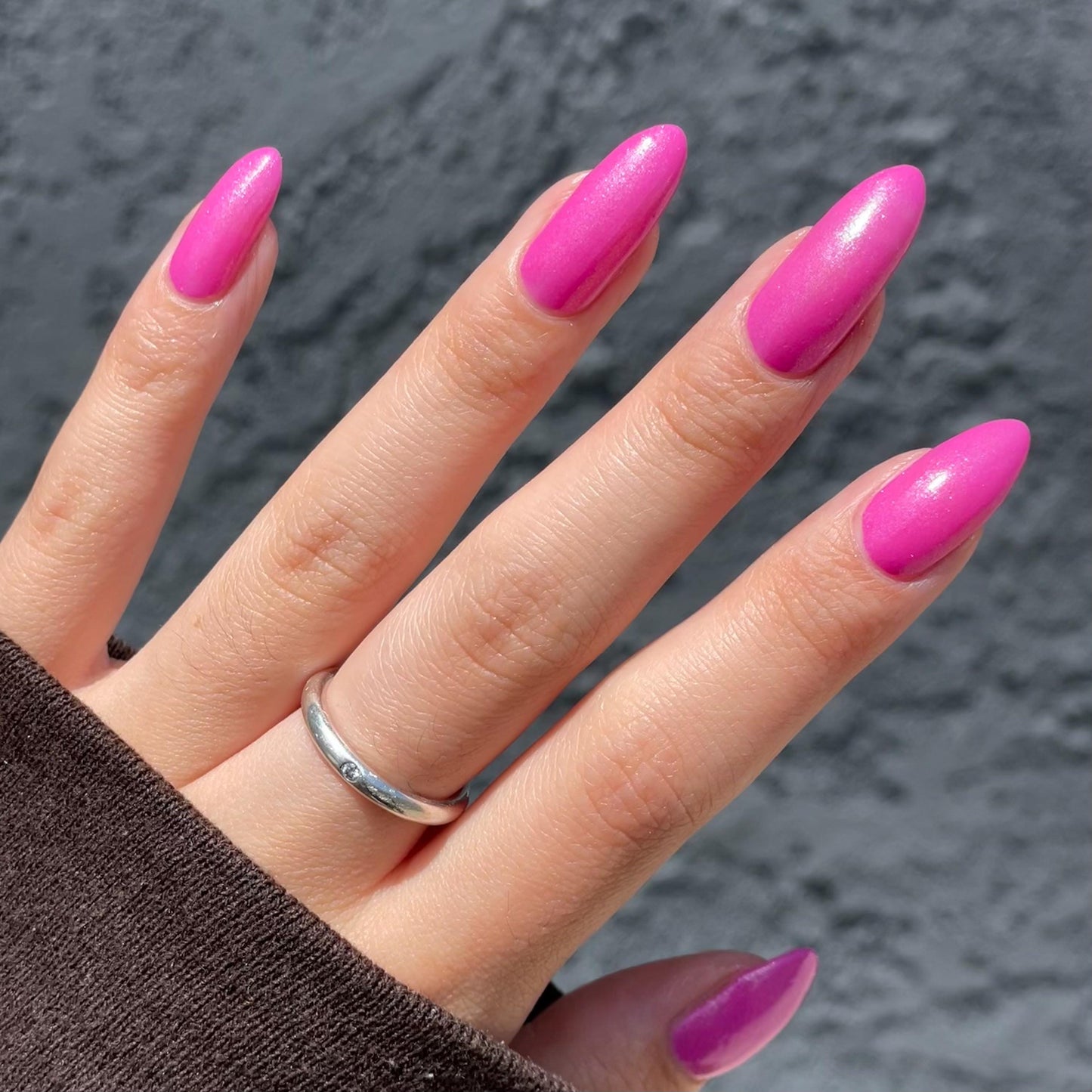 Long nails showcase a bright pink with a slight purple hue glittering in the sun.