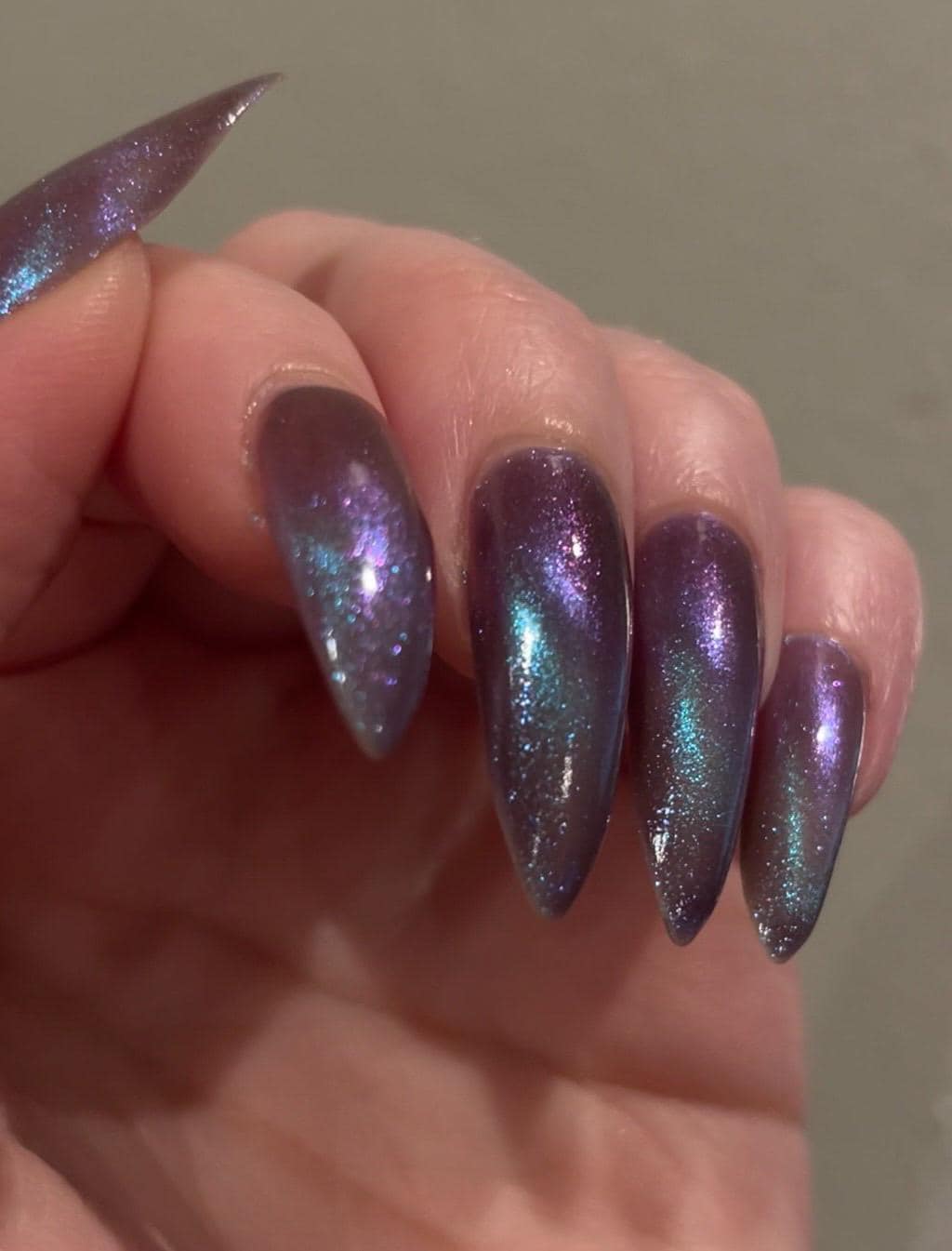 Long pointed nails are painted in a deep purple color that shimmers and sparkles with blue and purple magnetic particles. Magnetized in a stripe diagonally across the nails.