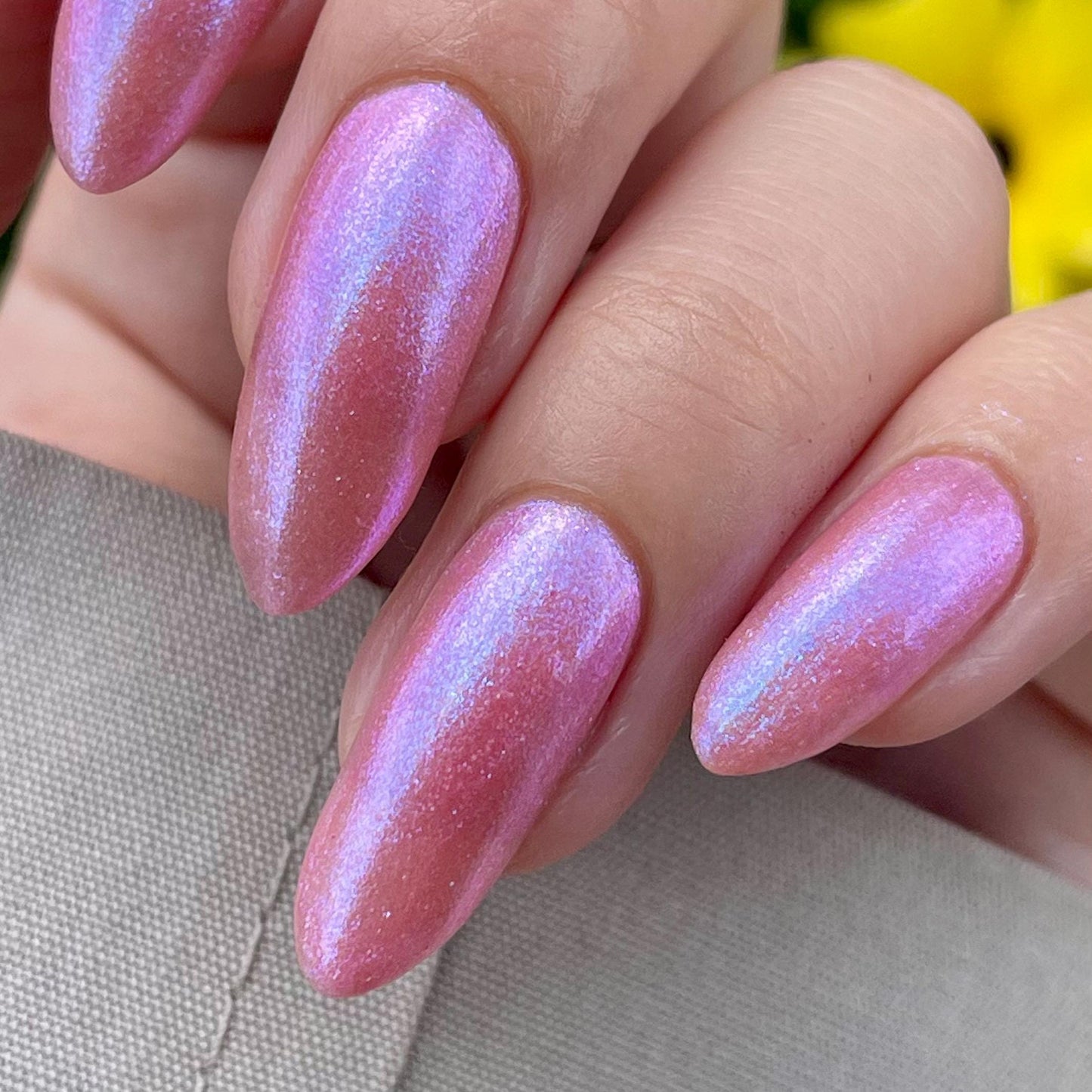 Elegant pale fingers end in long oval nails painted with a pale pink shimmer nail polish. The polish has blue to pink shifting shimmer and glows blue in the shaded light.