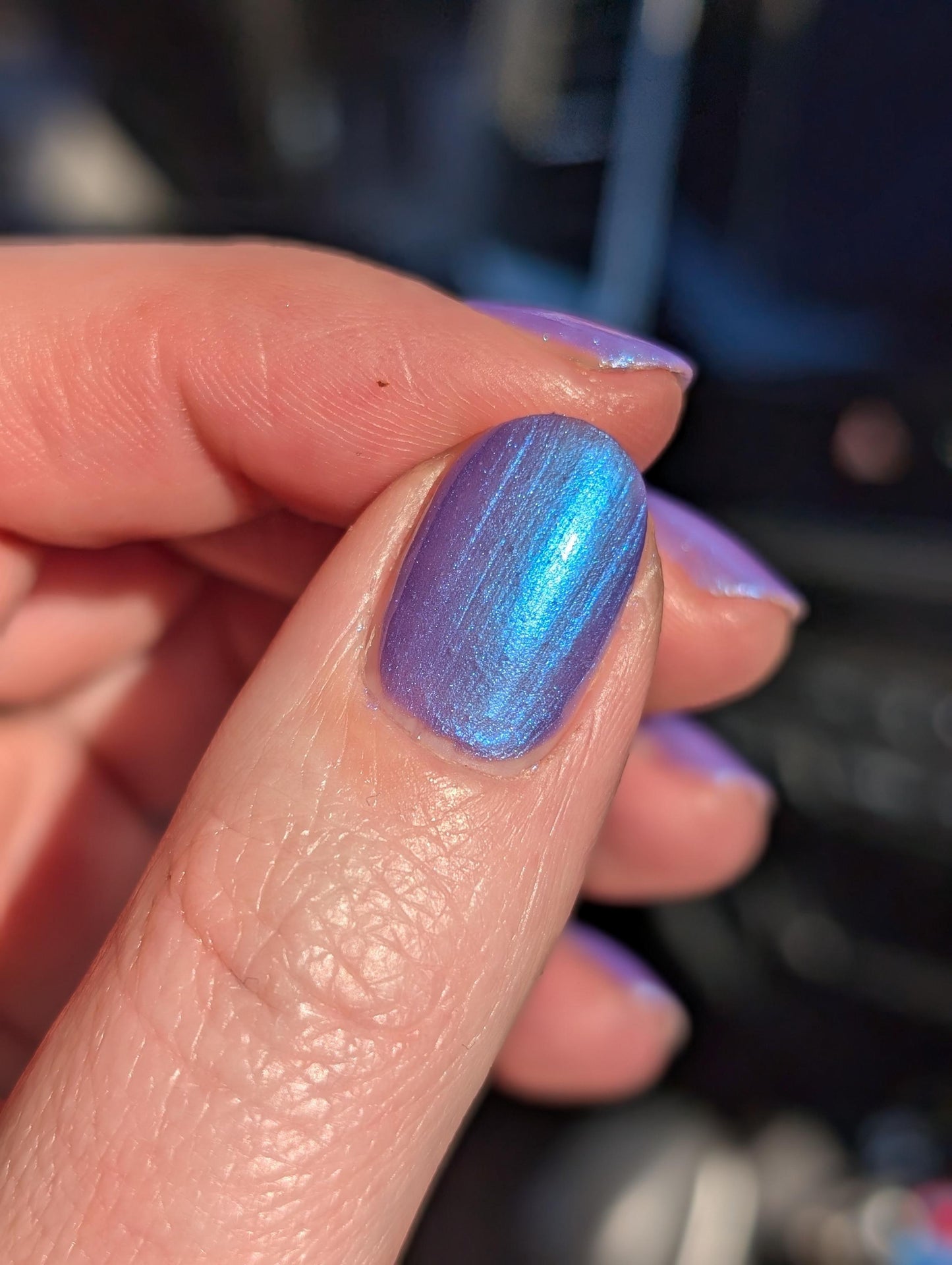 A closeup of a hand and nails displaying indigo polish with blue shimmer. Polish glows in the light.