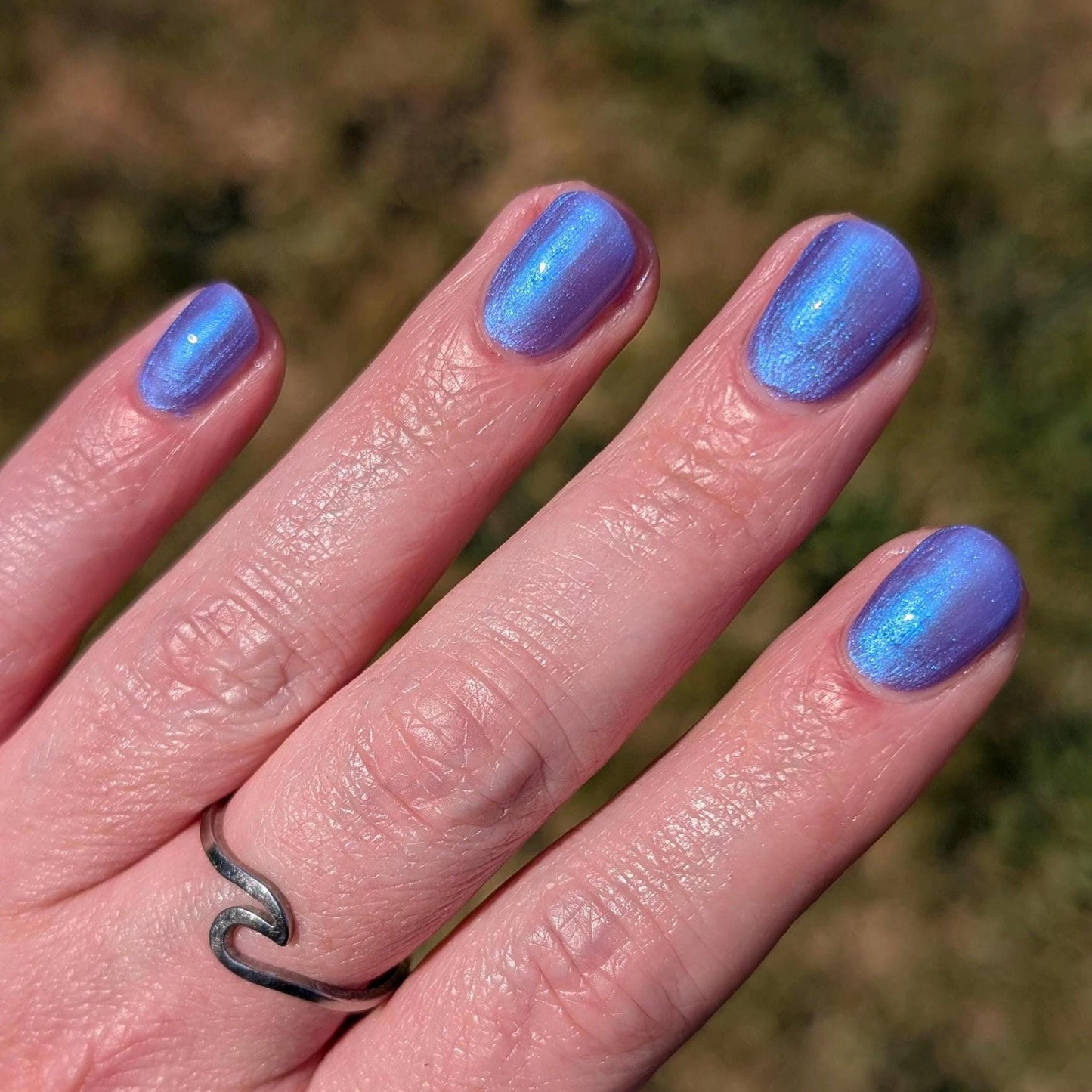 A closeup of a hand and nails displaying indigo polish with blue shimmer. Polish glows in the light.