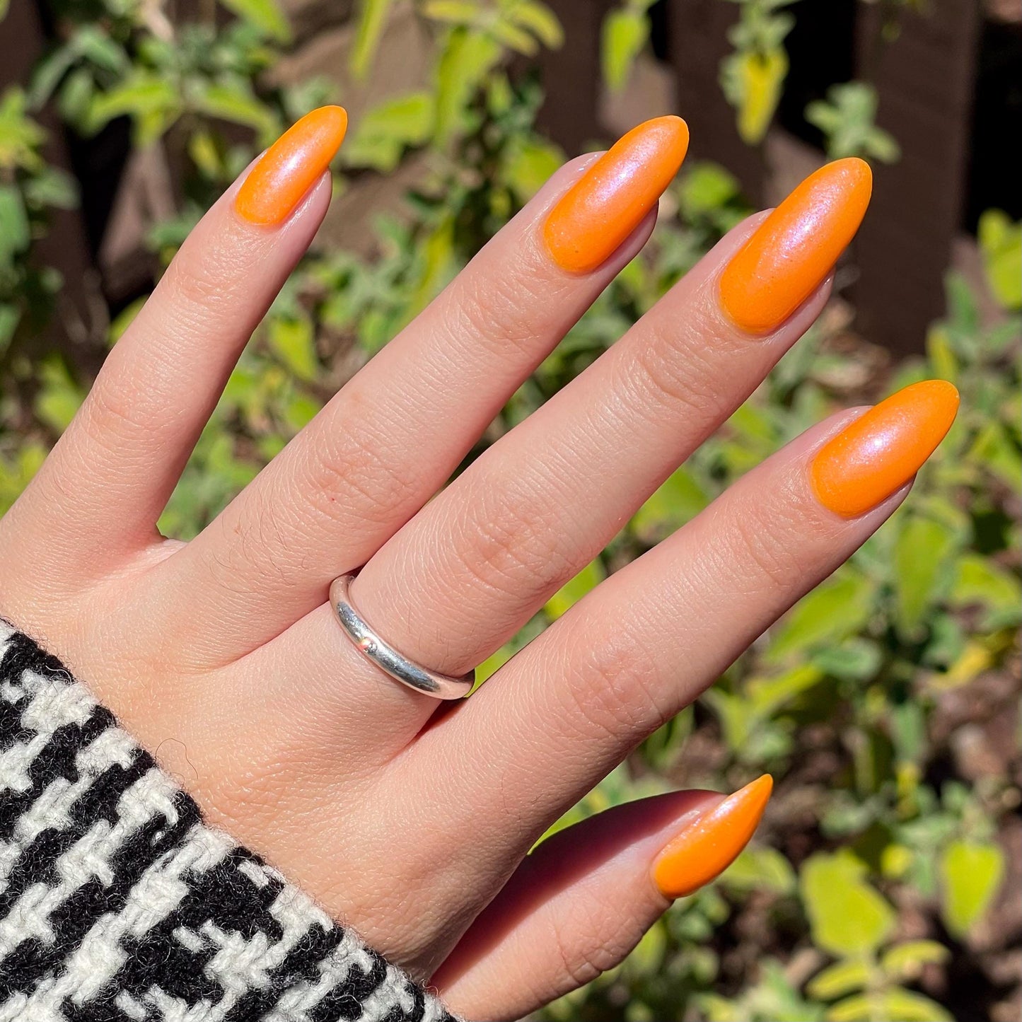 A closeup of a hand with nails painted neon orange nail lacquer with pink-purple shimmer.