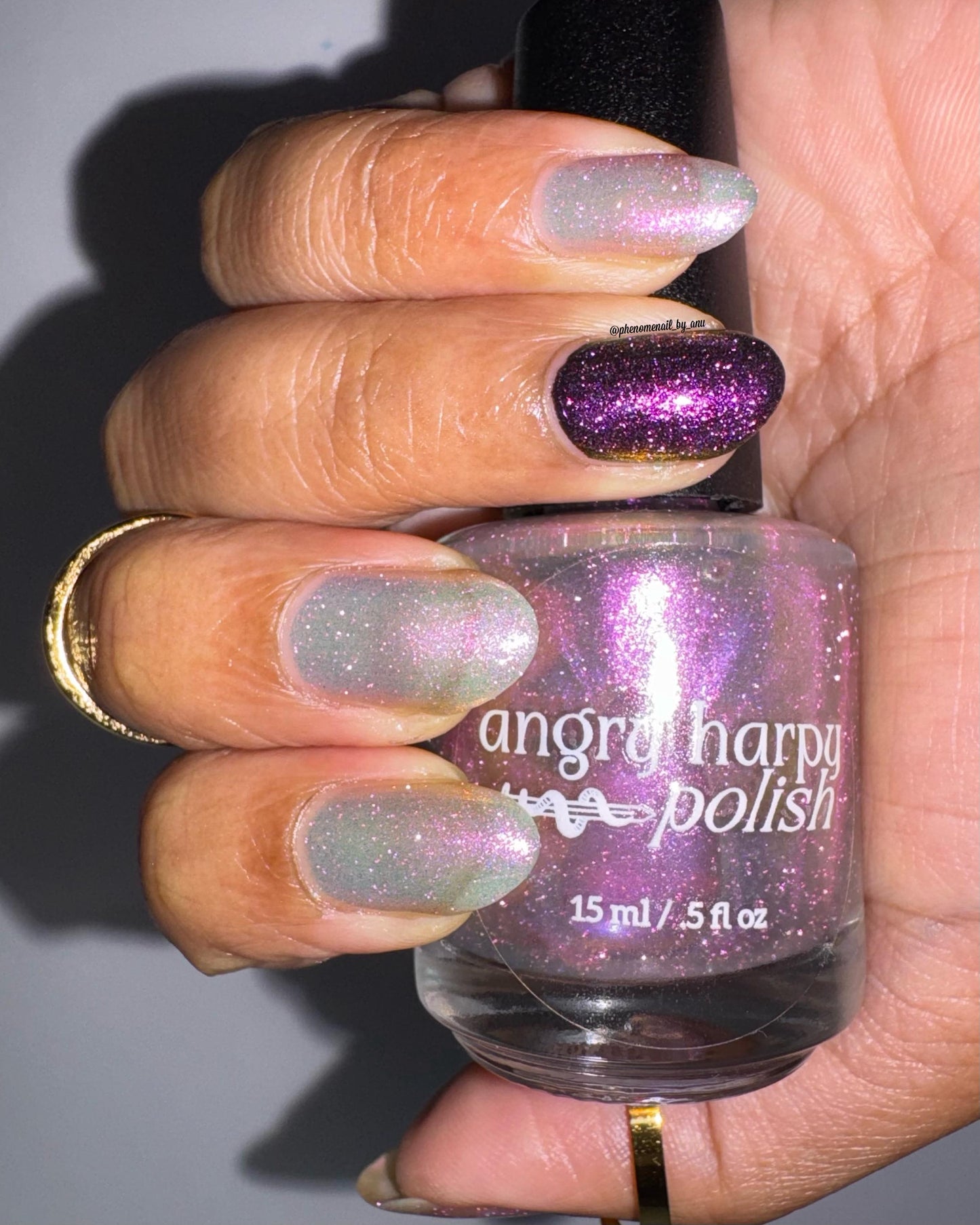 A closeup of a hand with nails painted a sheer multichrome nail polish that shifts gold-orange-pink-fuschia, with pale pink reflective glitter scattered throughout.