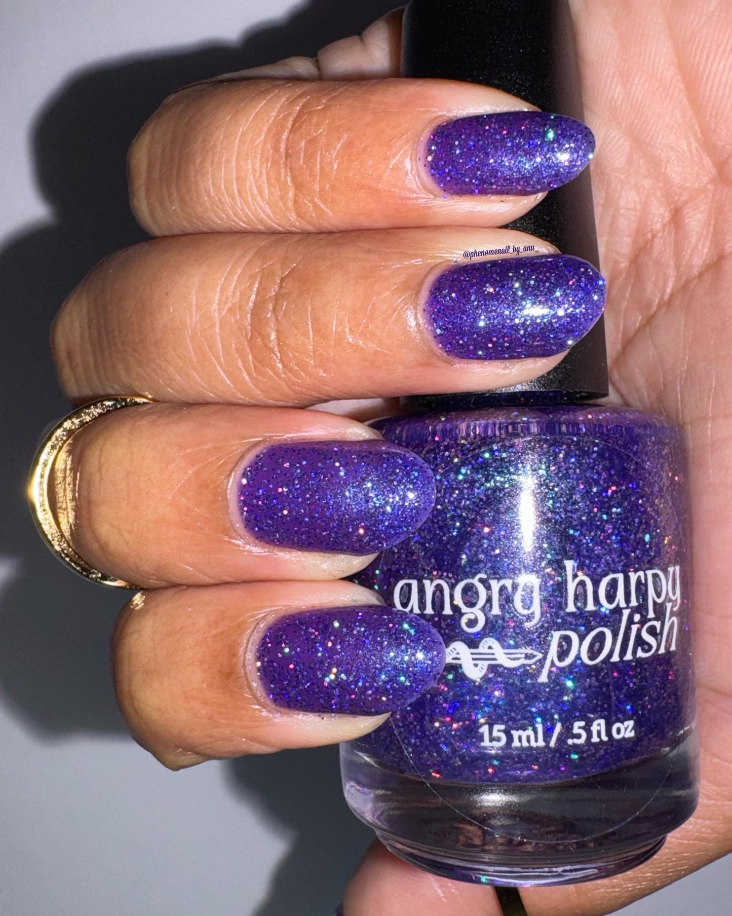 A closeup of a hand with nails painted a vibrant violet lacquer sparkling with purple holographic glitter and green shimmer. Glitter really sparkles in the flash lighting.