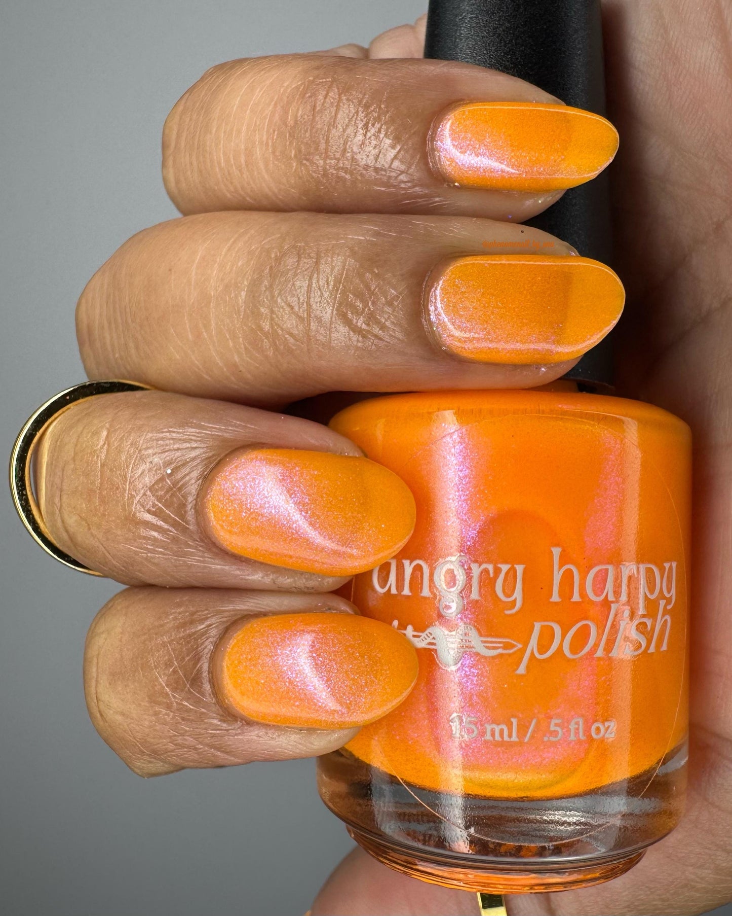 A closeup of a hand with nails painted neon orange nail lacquer with pink-purple shimmer.