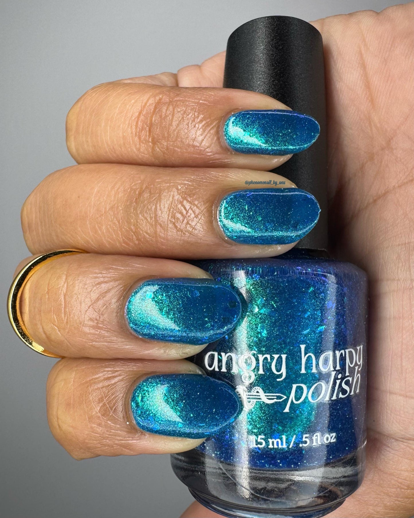A closeup of a medium-toned hand with nails painted a gorgeous, vibrant, shimmery deep teal color, packed with flakes and reflective blue glitter scattered throughout.