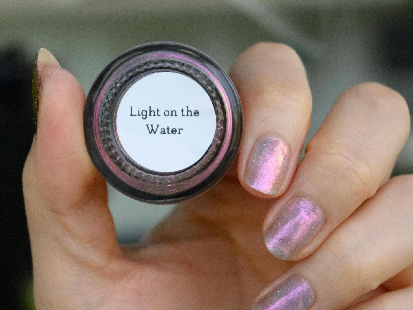 A closeup of a hand with nails painted a sheer multichrome nail polish that shifts gold-orange-pink-fuschia, with pale pink reflective glitter scattered throughout.