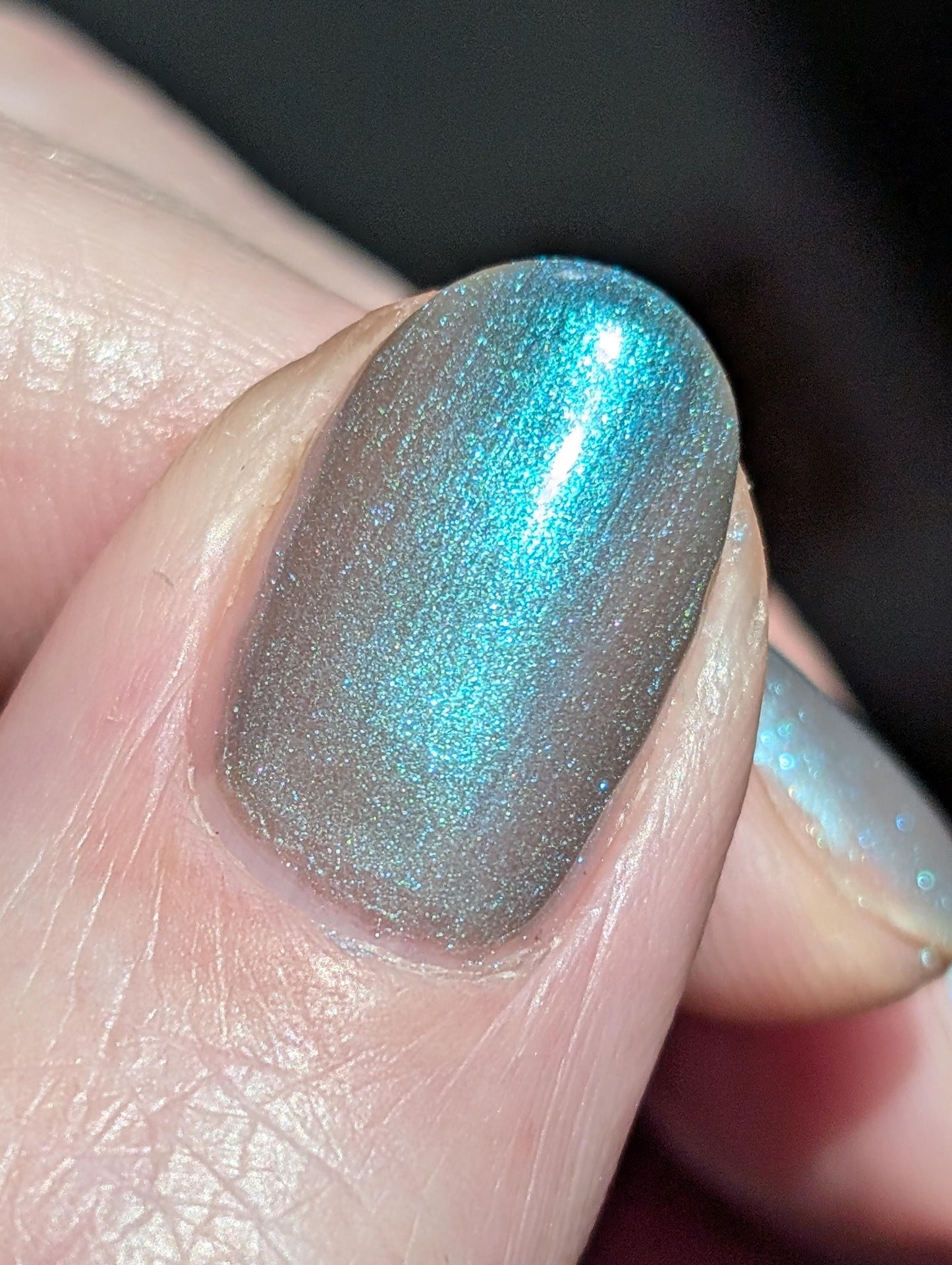 A closeup of a hand with nails painted an ethereal gray with bright, glowy turquoise shimmer.