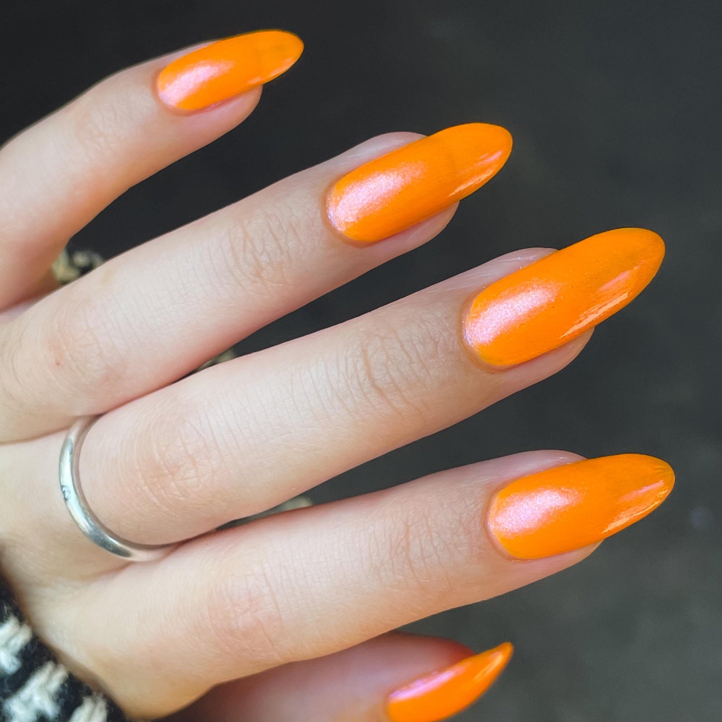 A closeup of a hand with nails painted neon orange nail lacquer with pink-purple shimmer.