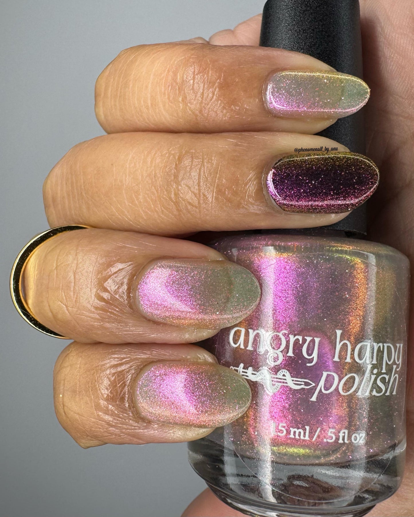 A closeup of a hand with nails painted a sheer multichrome nail polish that shifts gold-orange-pink-fuschia, with pale pink reflective glitter scattered throughout.