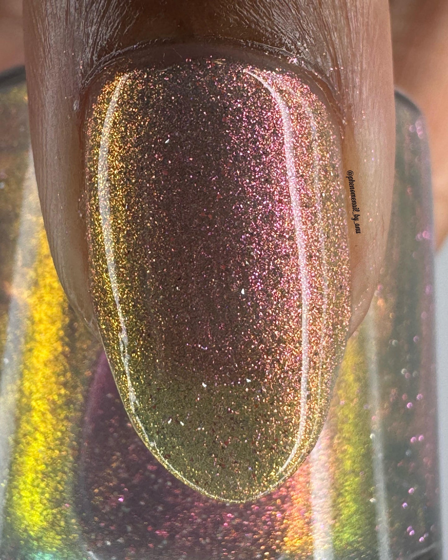 A closeup of a thumbnail painted a sheer multichrome nail that shifts gold-orange-pink-fuschia, with pale pink reflective glitter scattered throughout.