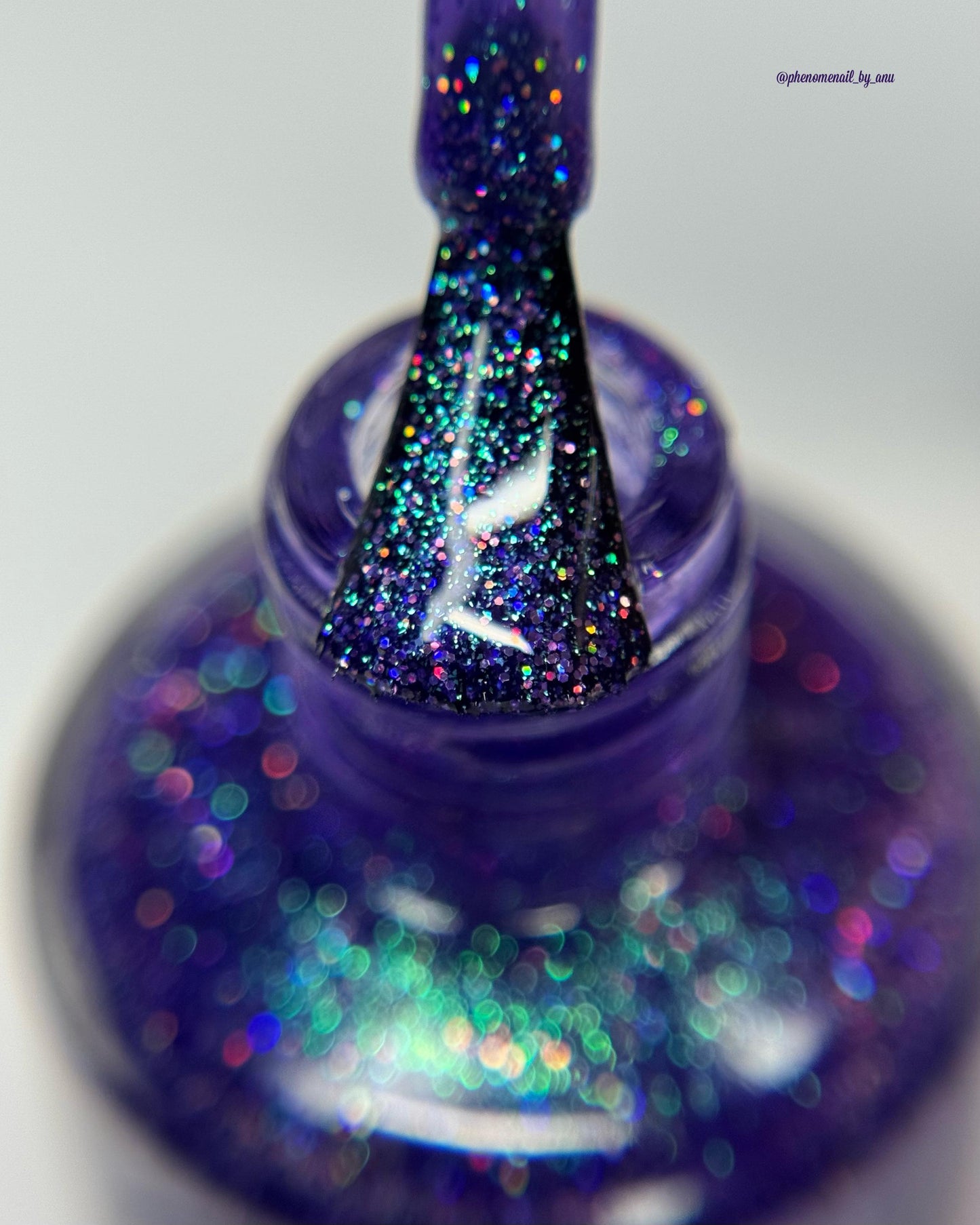 A closeup of a nail bottle brush coated in a vibrant violet lacquer sparkling with purple holographic glitter and green shimmer.