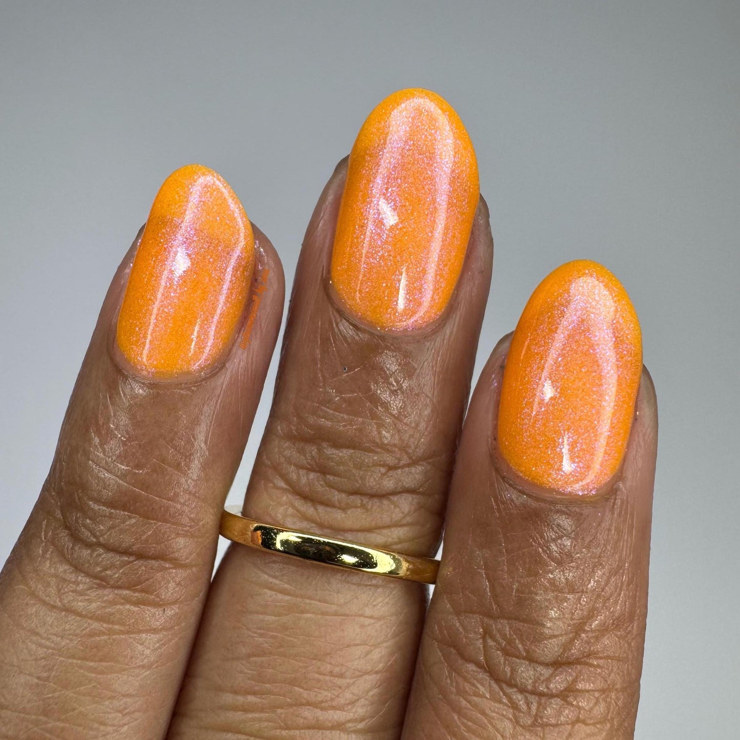 A closeup of three medium-brown fingers with nails painted neon orange nail lacquer with pink-purple shimmer.