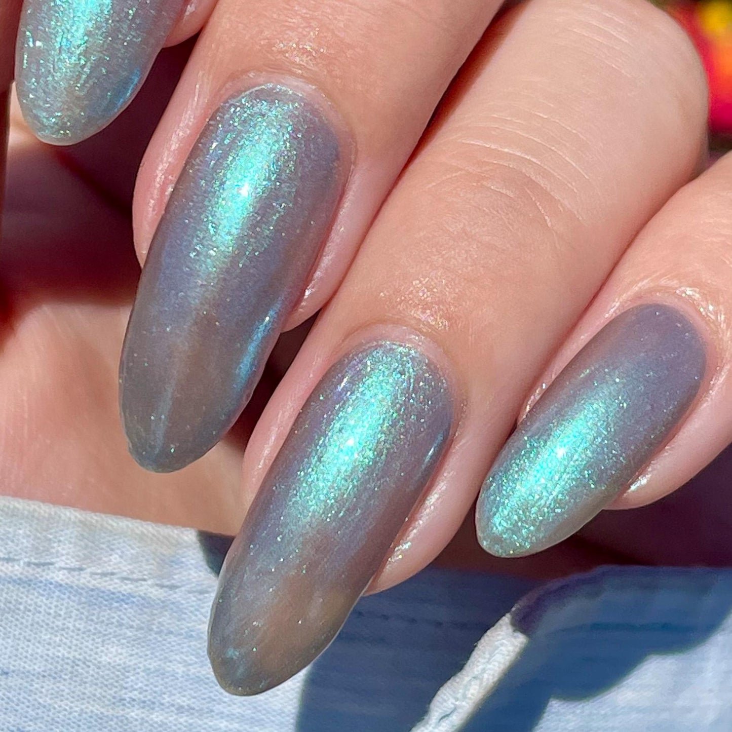 A closeup of a hand with nails painted an ethereal gray with bright, glowy turquoise shimmer.