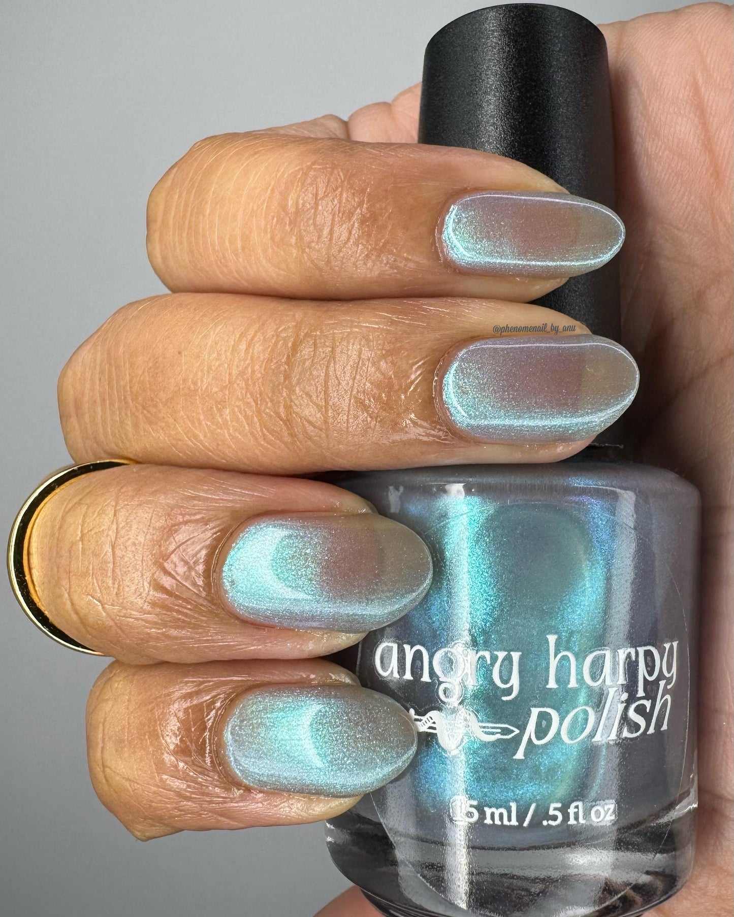 A closeup of a hand with nails painted an ethereal gray with bright, glowy turquoise shimmer.