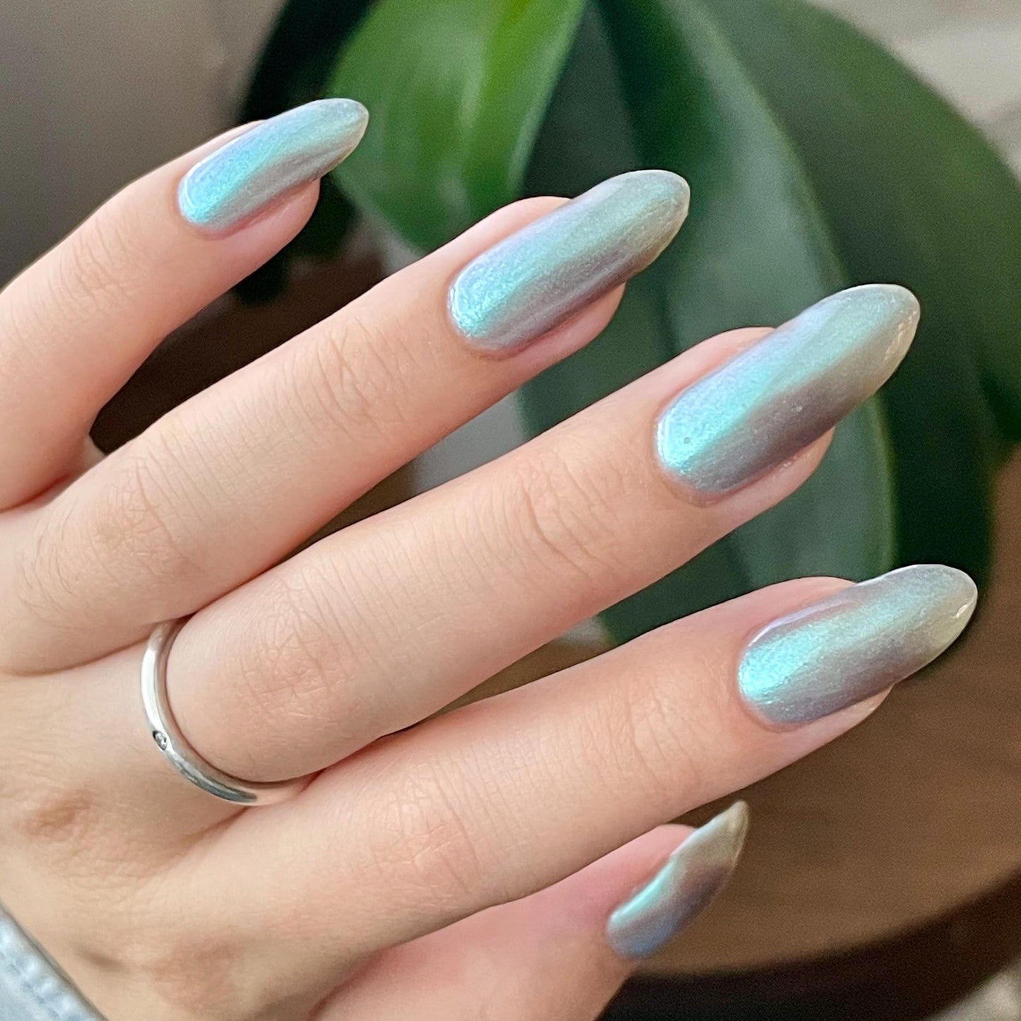 A closeup of a hand with nails painted an ethereal gray with bright, glowy turquoise shimmer.
