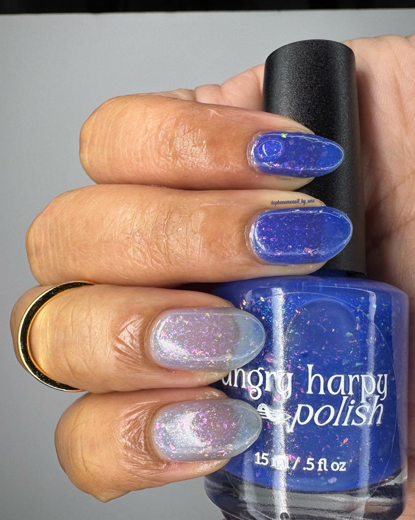 A closeup of a hand with nails painted a thermal polish that goes from dark blue (cold) to a blue-tinted clear (warm). Polish is filled with iridescent green-pink flakes and blue shimmer.