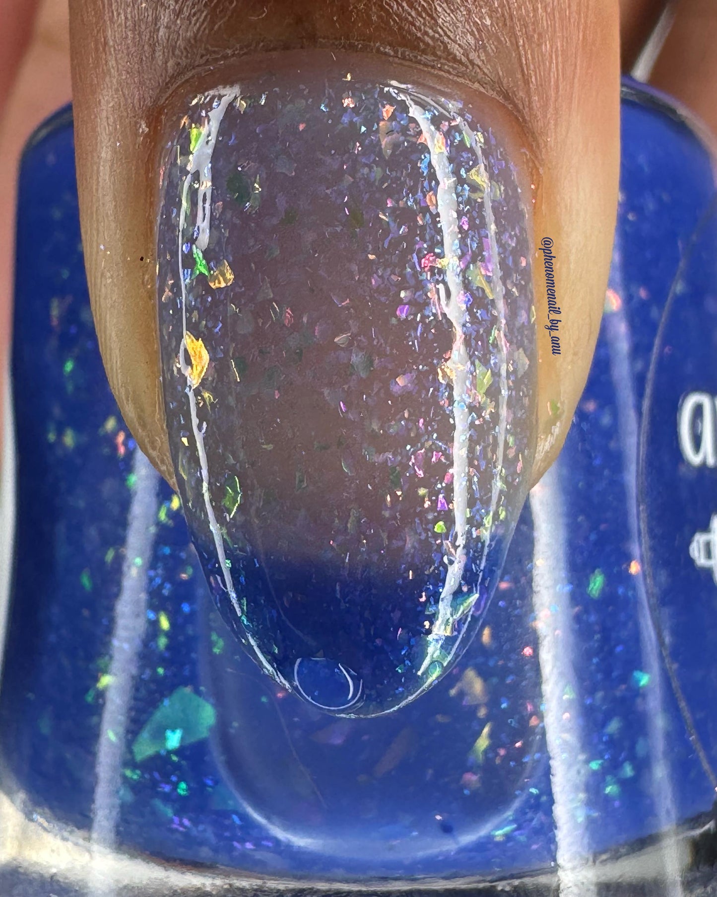 A closeup of a thumbnail painted a thermal polish that goes from dark blue at the tips (cold) to a blue-tinted clear (warm). Polish is filled with iridescent green-pink flakes and blue shimmer.