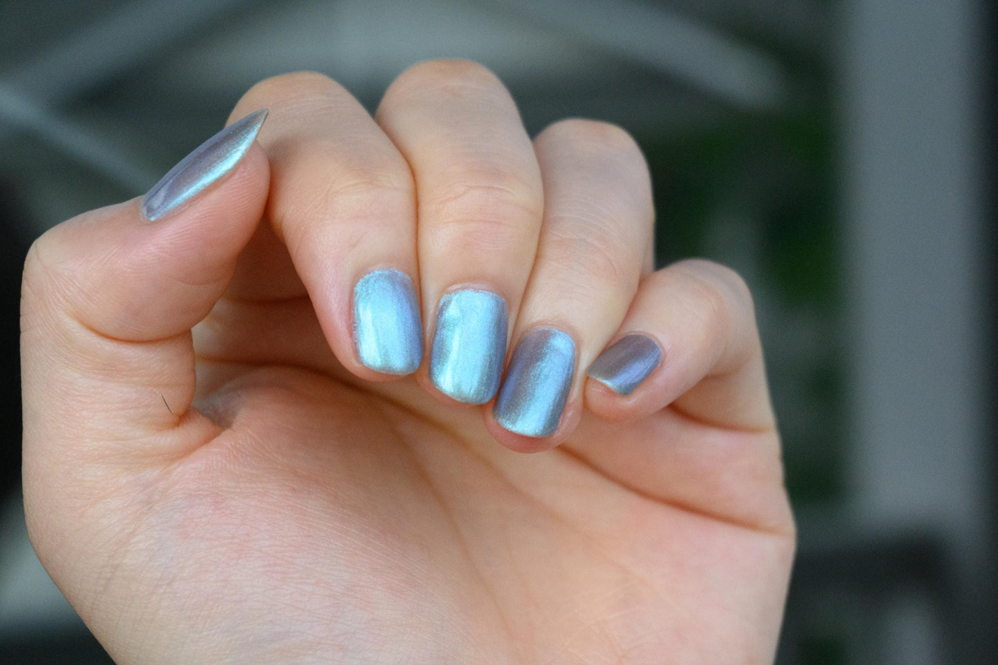 A closeup of a hand with nails painted an ethereal gray with bright, glowy turquoise shimmer.