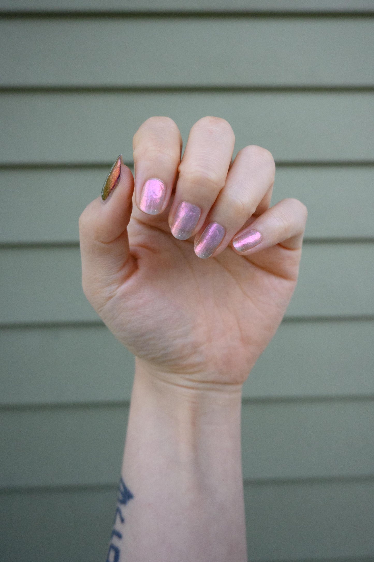 A closeup of a hand with nails painted a sheer multichrome nail polish that shifts gold-orange-pink-fuschia, with pale pink reflective glitter scattered throughout.