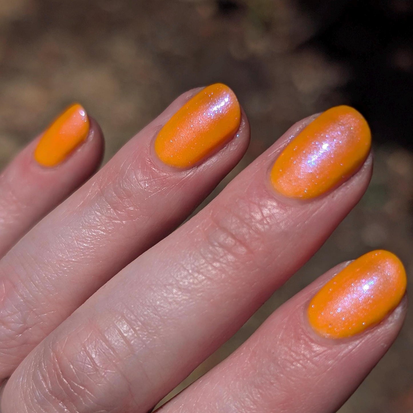 A closeup of a hand with nails painted neon orange nail lacquer with pink-purple shimmer.
