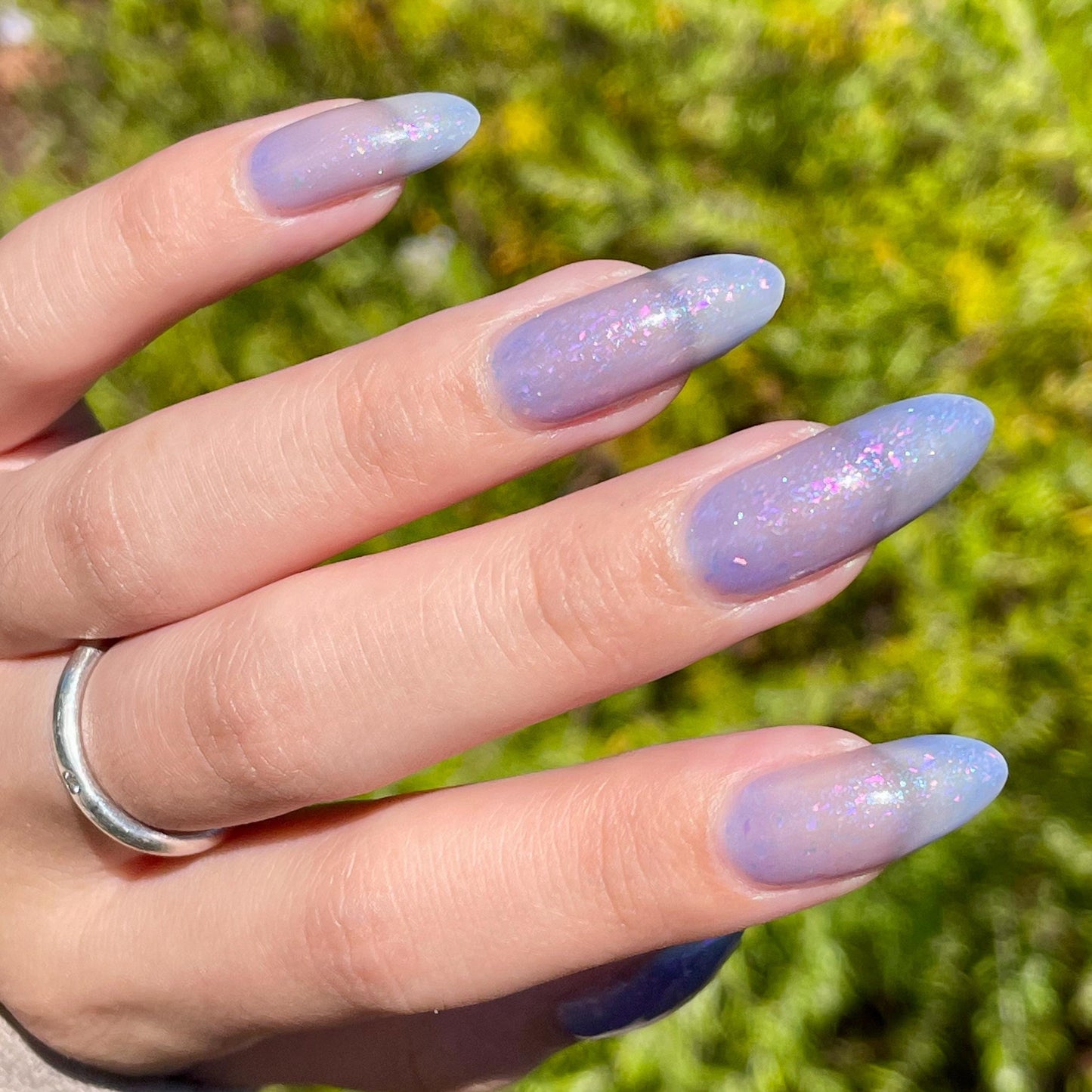 A closeup of a hand with nails painted a thermal polish in its warm state - a blue-tinted clear. The lacquer is filled with iridescent green-pink flakes and blue shimmer.