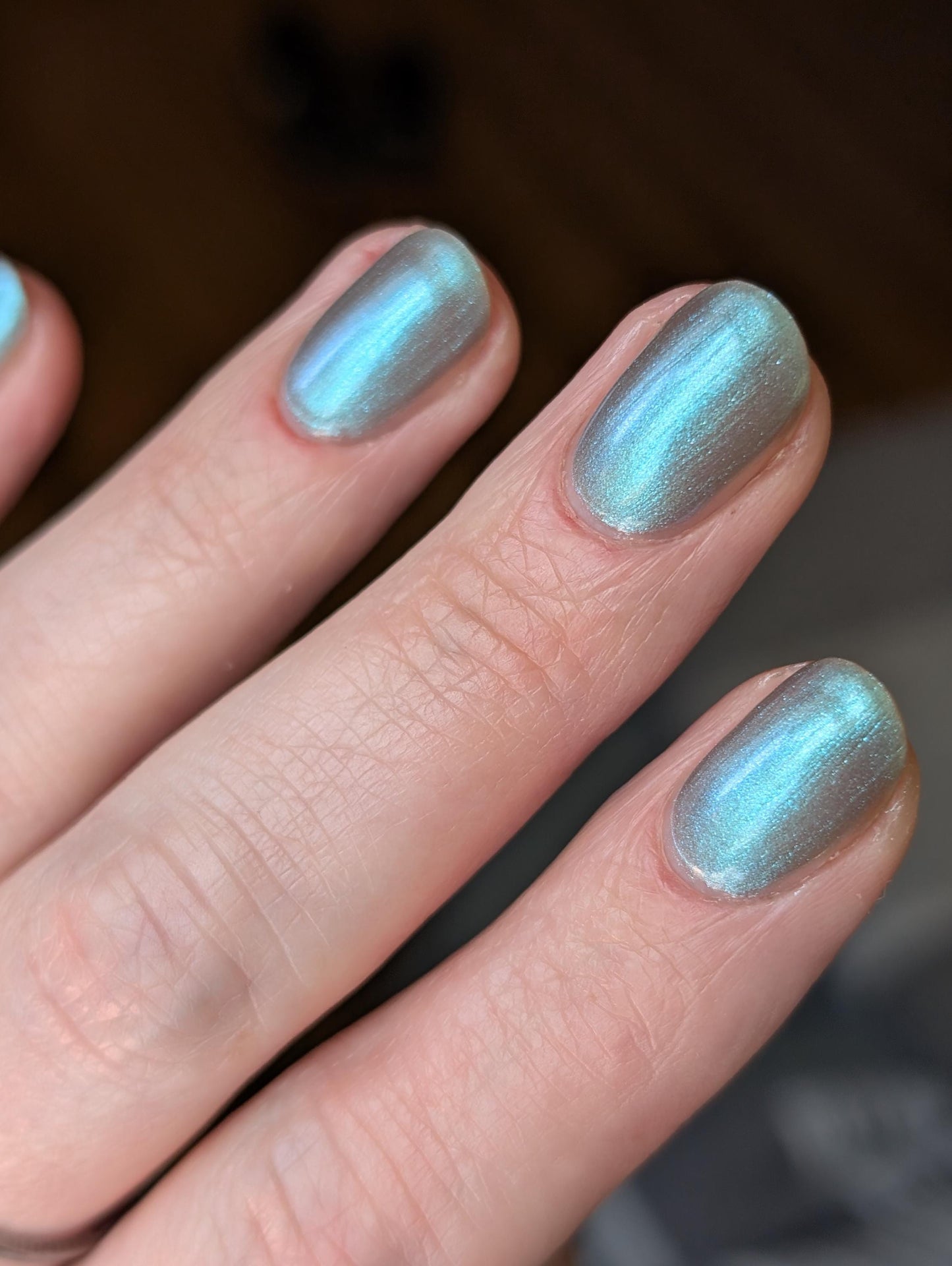 A closeup of a hand with nails painted an ethereal gray with bright, glowy turquoise shimmer.