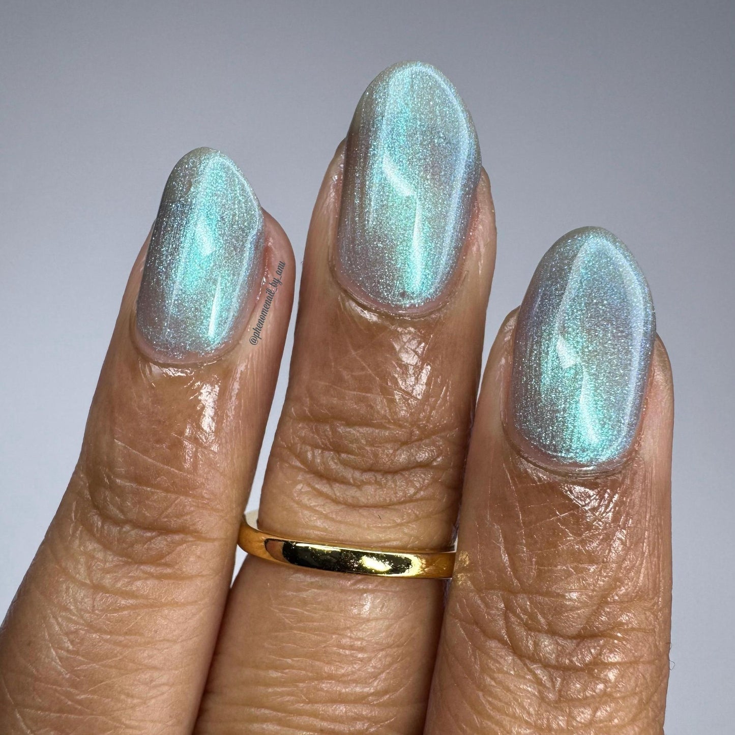 A closeup of a hand with nails painted an ethereal gray with bright, glowy turquoise shimmer.