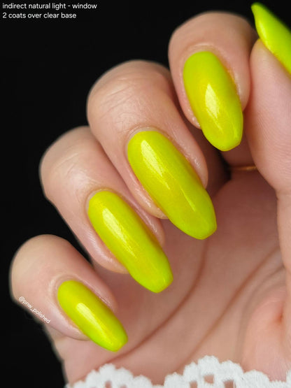 Close-up of a hand with long almond-shaped nails painted in a bright neon yellow-green polish, shown against a black background with small text in the upper left.