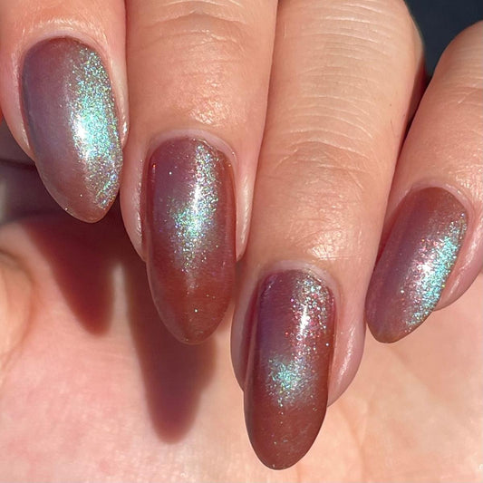 Close-up of a hand with manicured nails painted in a shimmery orange-brown polish with teal magnetic pigment.