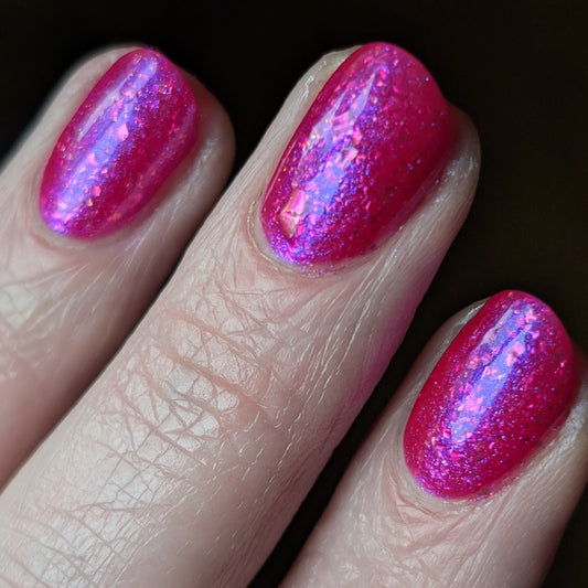 Close-up of a hand with pink glittery nail polish on a dark background