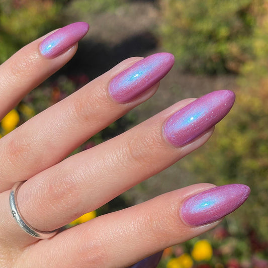 A hand with long nails is painted a purple mauve color with blue shimmer that appears to glow in the sunlight.