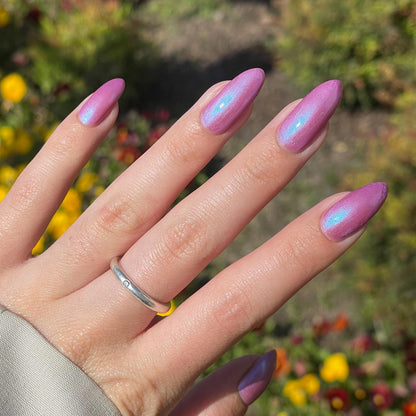 A hand with long nails is painted a purple mauve color with blue shimmer that appears to glow in the sunlight.