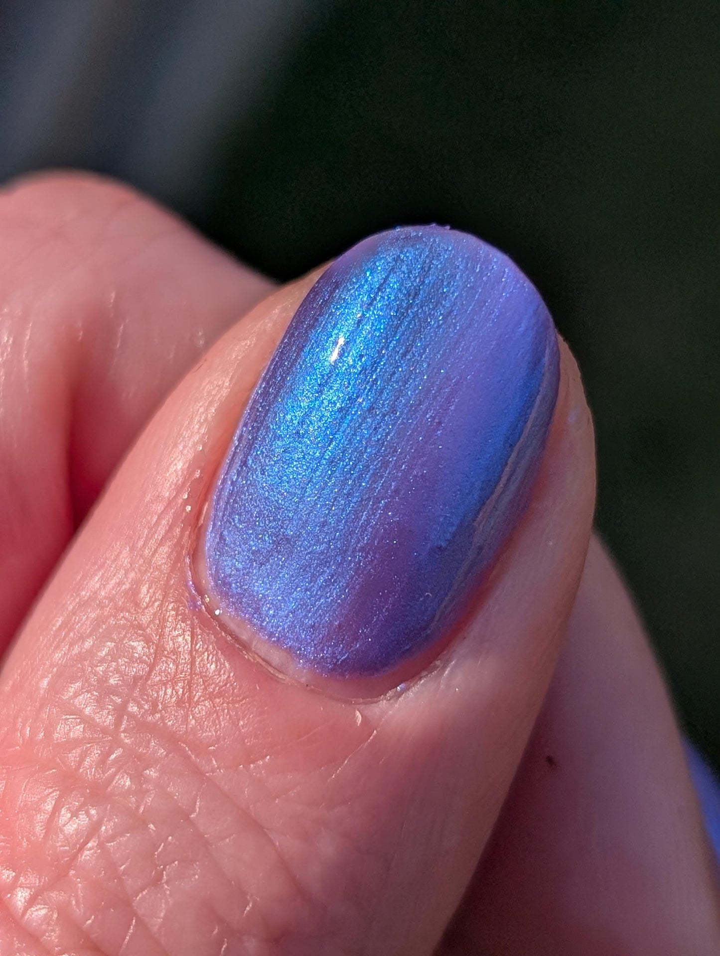 A closeup of a thumbnail displaying indigo polish with blue shimmer. Polish glows in the light.