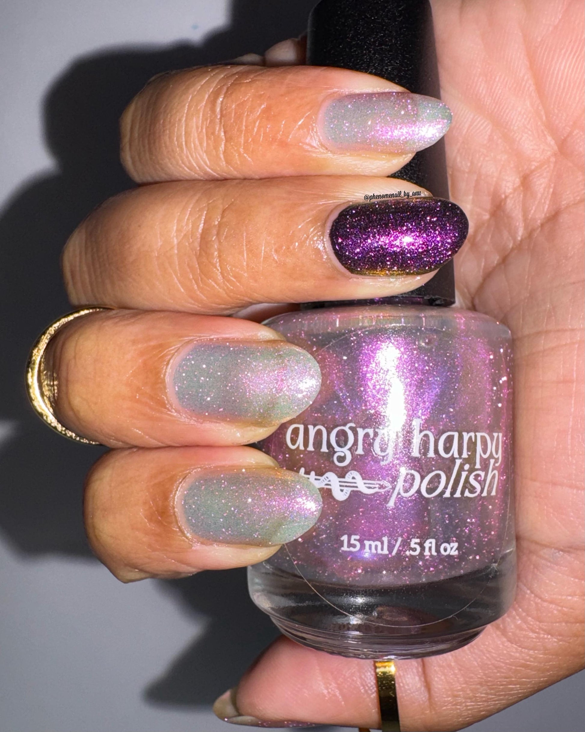 A closeup of a hand with nails painted a sheer multichrome nail polish that shifts gold-orange-pink-fuschia, with pale pink reflective glitter scattered throughout.