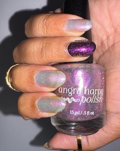 A closeup of a hand with nails painted a sheer multichrome nail polish that shifts gold-orange-pink-fuschia, with pale pink reflective glitter scattered throughout.