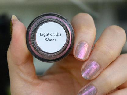 A closeup of a hand with nails painted a sheer multichrome nail polish that shifts gold-orange-pink-fuschia, with pale pink reflective glitter scattered throughout.
