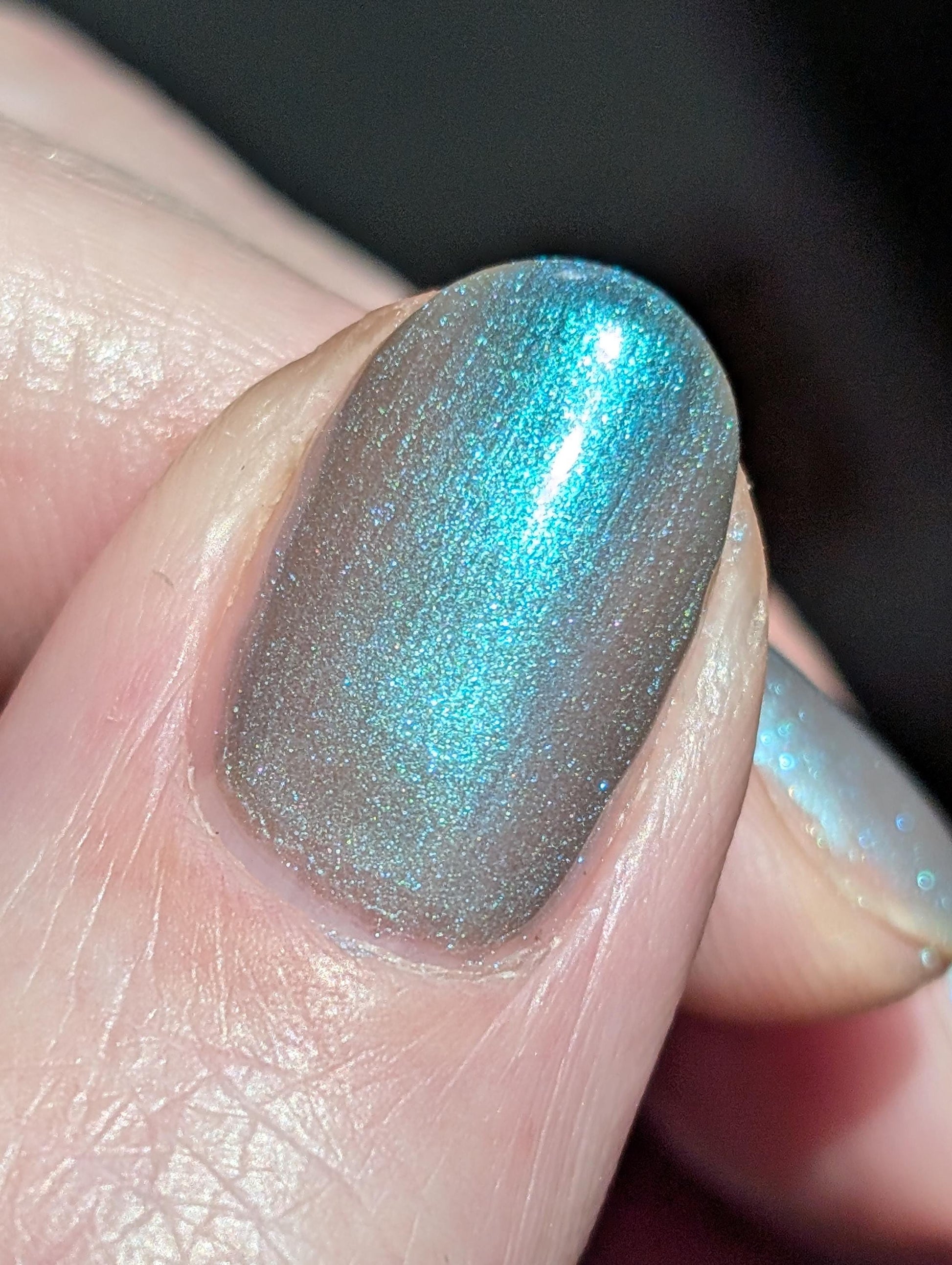 A closeup of a hand with nails painted an ethereal gray with bright, glowy turquoise shimmer.