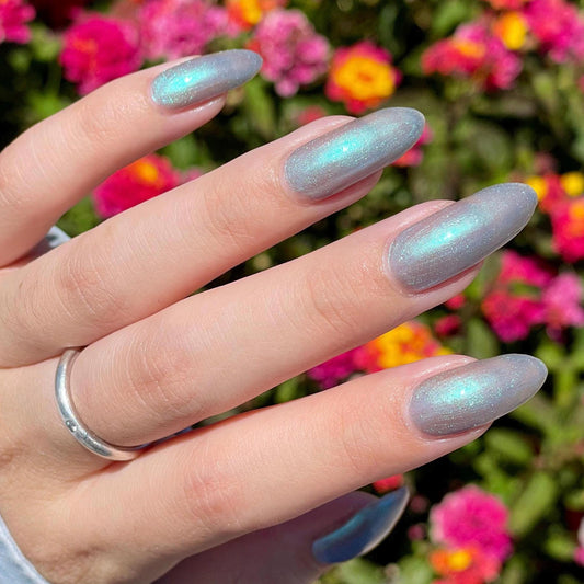 A closeup of a hand with nails painted an ethereal gray with bright, glowy turquoise shimmer.