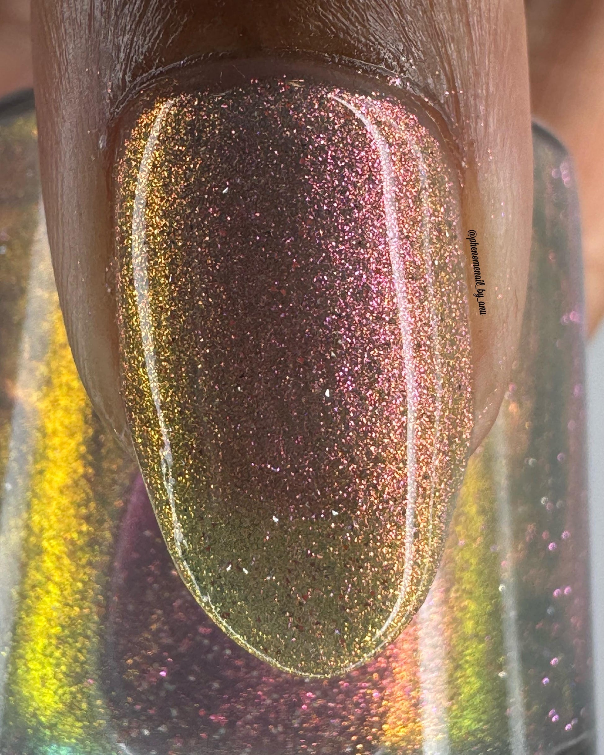 A closeup of a thumbnail painted a sheer multichrome nail that shifts gold-orange-pink-fuschia, with pale pink reflective glitter scattered throughout.
