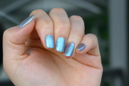 A closeup of a hand with nails painted an ethereal gray with bright, glowy turquoise shimmer.