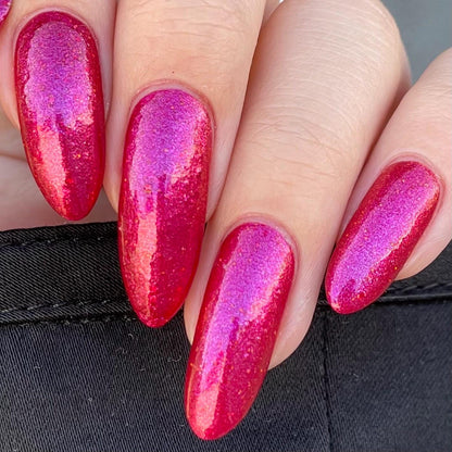 Closeup of nails painted in a lacquer that is bright red with an orange color shift and glitters.